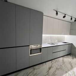 MeBle PRO - Nowoczesna kuchnia z szarymi matowymi frontami, wbudowanym piekarnikiem i marmurowym blatem oraz podświetleniem LED pod szafkami wiszącymi.