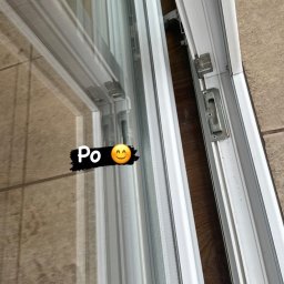 My clean team - Błyszcząca, czysta szyba okienna z białymi ramami, widoczne okucia i mechanizm otwierania, odbicie podłogi w szybie.