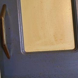 My clean team - Brudny, kremowy front kuchenny z metalowym uchwytem przed czyszczeniem, widoczne liczne plamy i zabrudzenia, ujęcie z bliska.