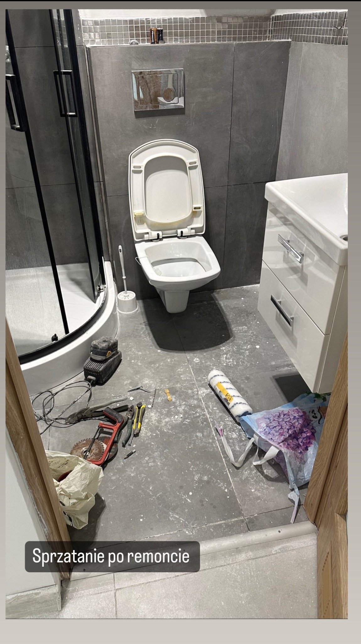 Łazienka w trakcie prac wykończeniowych: otwarta toaleta, prysznic, umywalka z szafką, narzędzia i akcesoria malarskie na podłodze.
