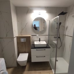 MARIUSZ STRZELAK - Nowoczesna łazienka w Sokółce z kabiną prysznicową typu walk-in, umywalką nablatową na szafce z szufladami, podwieszaną toaletą i lustrem okrągłym z podświetleniem LED.