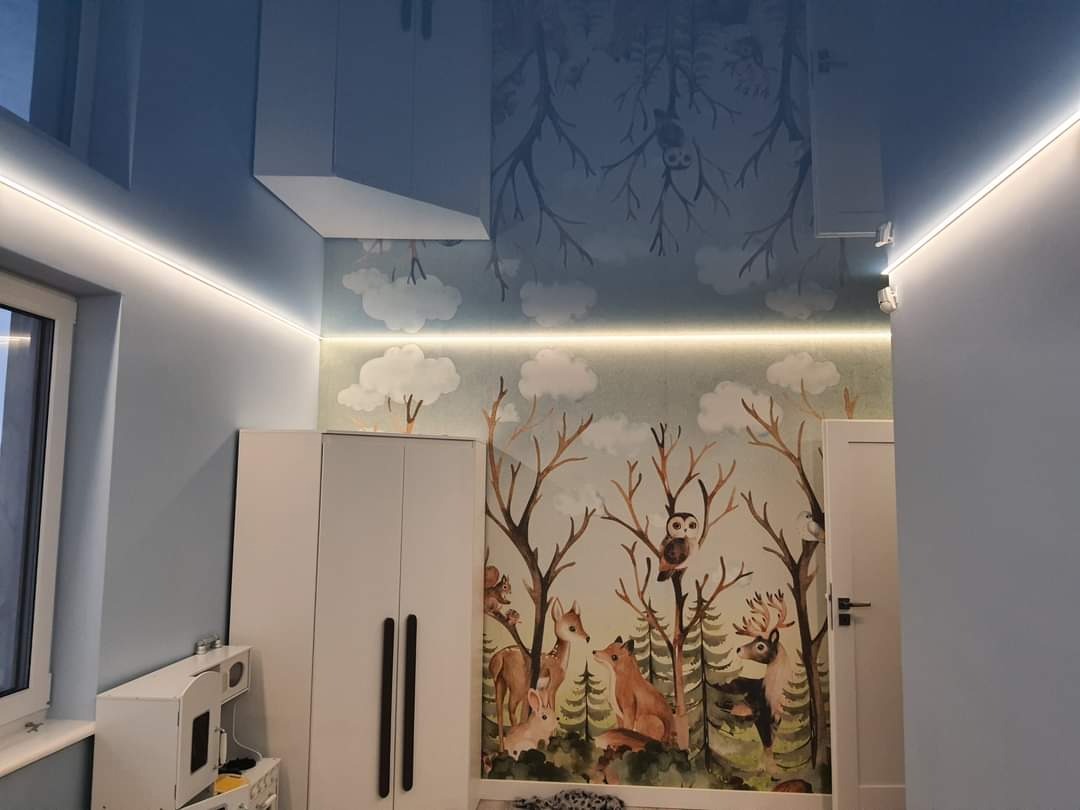 Pokój dziecięcy z fototapetą leśną, podświetlanym sufitem napinanym i meblami w kolorze złamanej bieli.