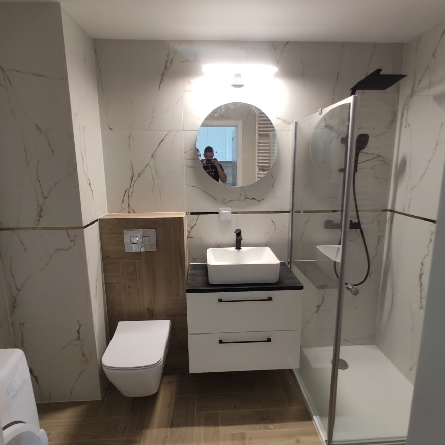 Nowoczesna łazienka w Sokółce z kabiną prysznicową typu walk-in, umywalką nablatową na szafce z szufladami, podwieszaną toaletą i lustrem okrągłym z podświetleniem LED.