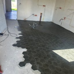 Pavlo Zhosan - Układanie heksagonalnych płytek podłogowych w pomieszczeniu w trakcie prac wykończeniowych, widoczne przewody elektryczne w ścianach.