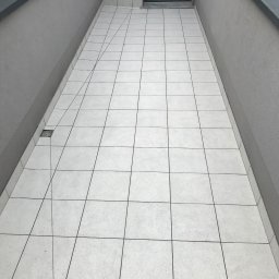 Pavlo Zhosan - Wyłożony jasnymi płytkami taras z odpływem liniowym przy ścianie, widok z góry, szare ściany i metalowe obramowanie.