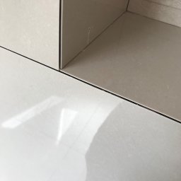 Pavlo Zhosan - Fragment narożnika wykończonego jasnymi, błyszczącymi płytkami ceramicznymi; widoczne fugi i subtelne refleksy światła.