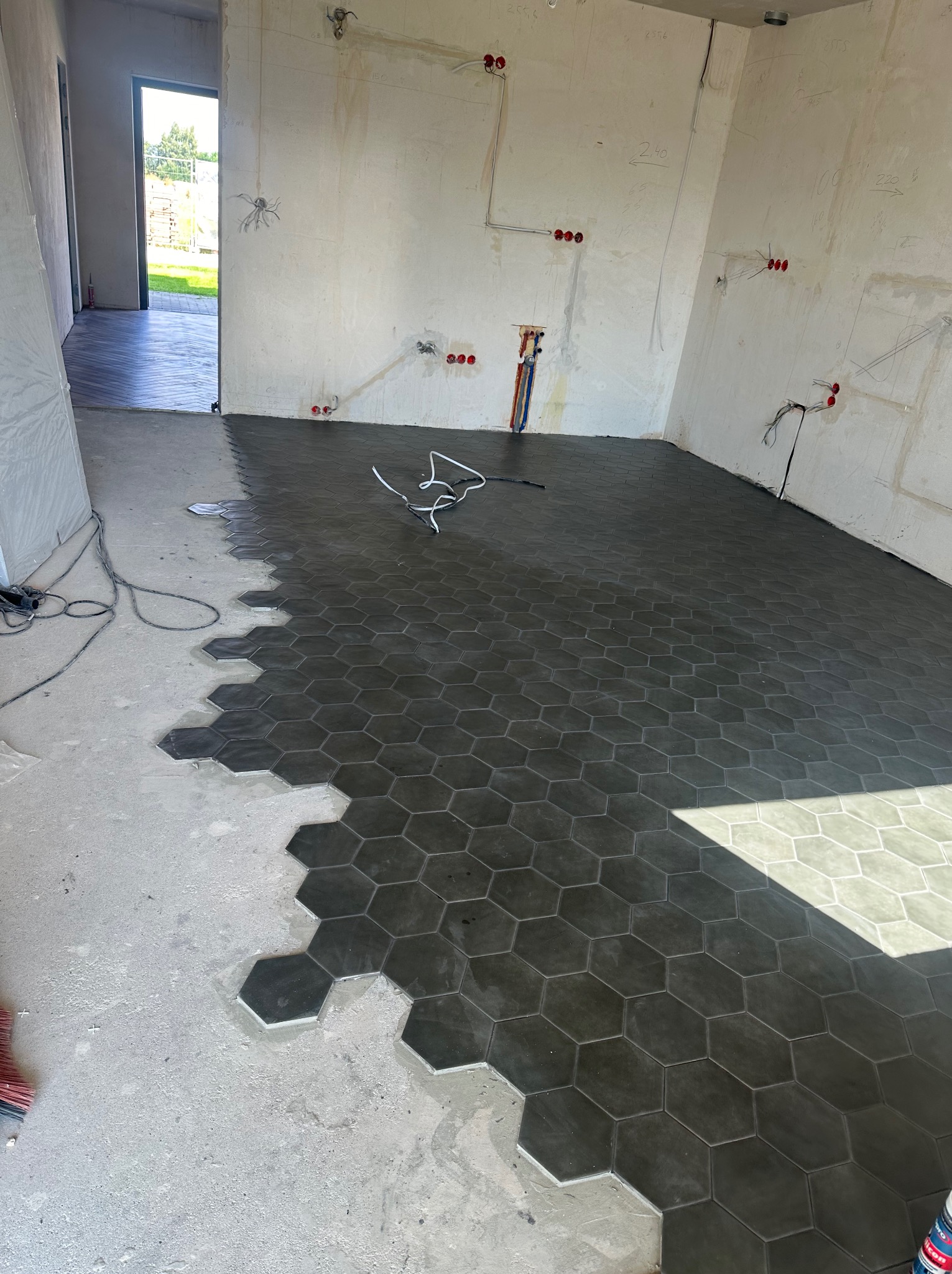 Układanie heksagonalnych płytek podłogowych w pomieszczeniu w trakcie prac wykończeniowych, widoczne przewody elektryczne w ścianach.