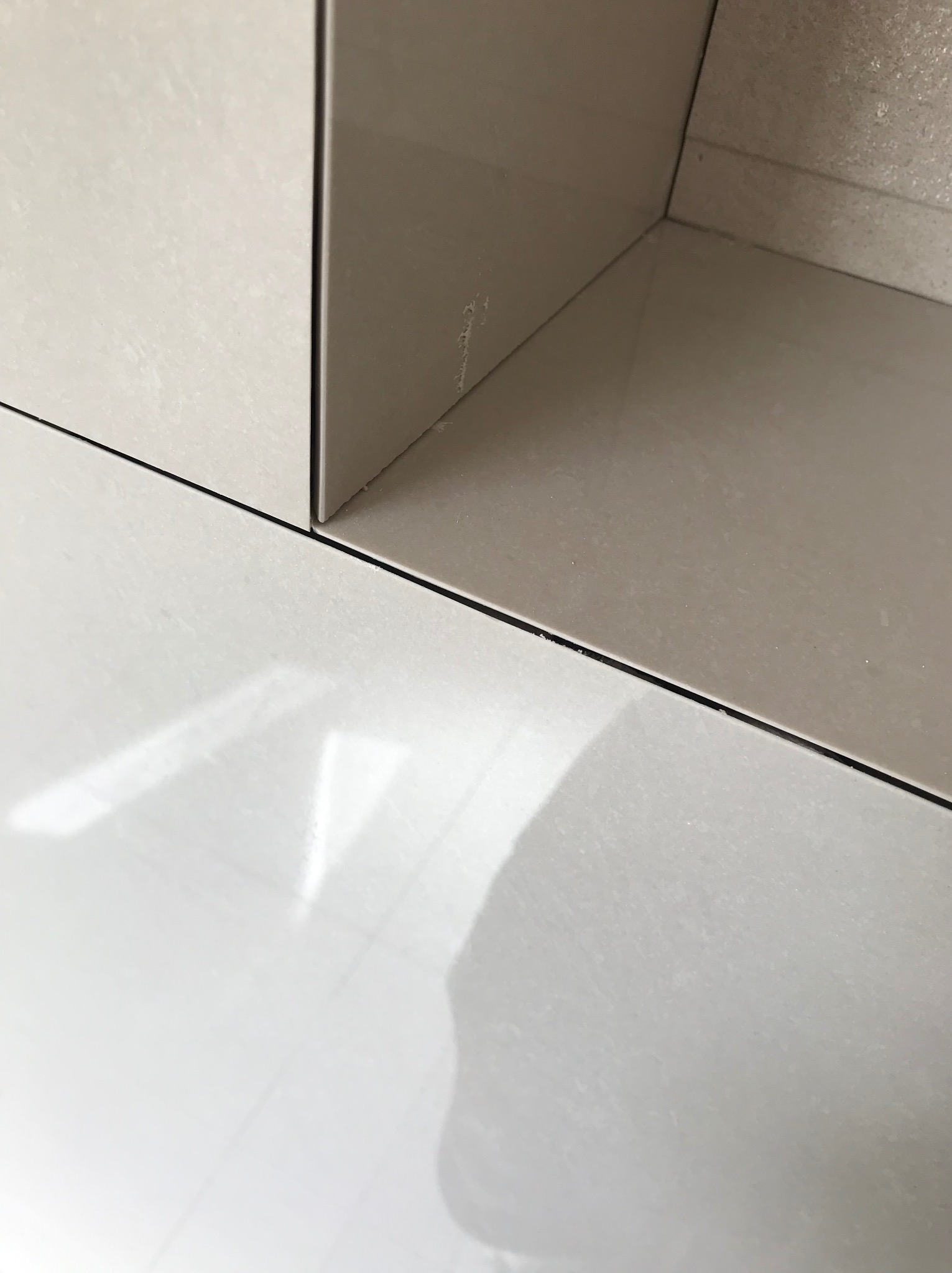 Fragment narożnika wykończonego jasnymi, błyszczącymi płytkami ceramicznymi; widoczne fugi i subtelne refleksy światła.