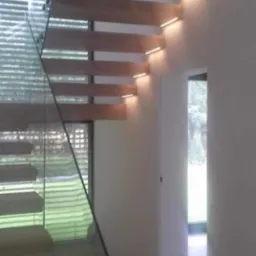 Nowoczesne schody drewniane z podświetleniem LED i szklaną balustradą, widok z dołu, minimalistyczny design.