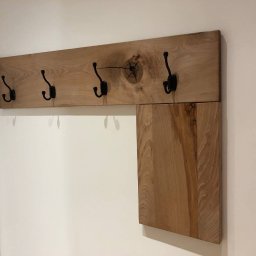 NaVo-Bud - Drewniany wieszak z pięcioma czarnymi haczykami, zamontowany na ścianie, z widocznym sękiem w drewnie i dodatkową półką z boku.