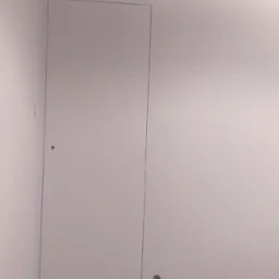 Świeżo pomalowane pomieszczenie z ukrytymi drzwiami i zabezpieczoną taśmą malarską górną krawędzią ściany oraz gniazdkiem elektrycznym w ścianie.