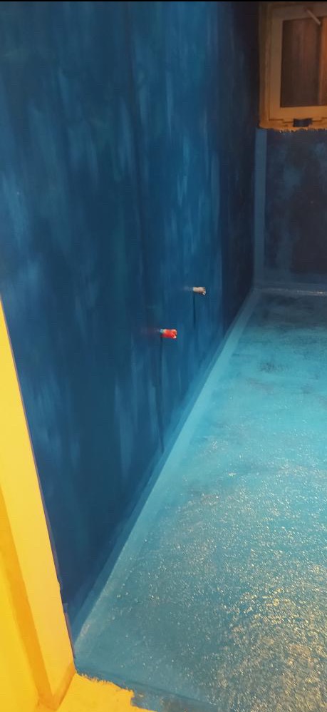 Niebieskie ściany i podłoga w trakcie prac wykończeniowych w pomieszczeniu z widocznymi rurami i oknem.