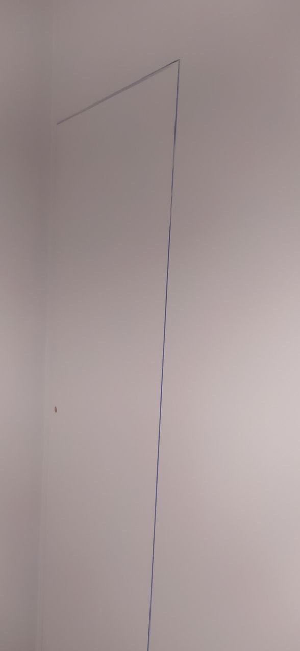 Świeżo pomalowana ściana w rogu pokoju, zabezpieczona taśmą malarską wzdłuż sufitu i ściany bocznej, widoczny niewielki ślad po szpachlowaniu.