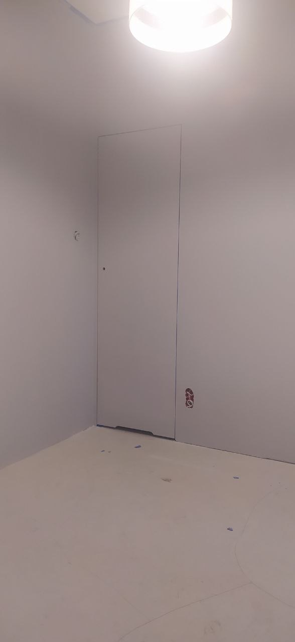 Pokój po świeżym malowaniu na jednolity, jasny kolor, widoczna ukryta futryna drzwiowa i wystające przewody elektryczne w dolnej części ściany