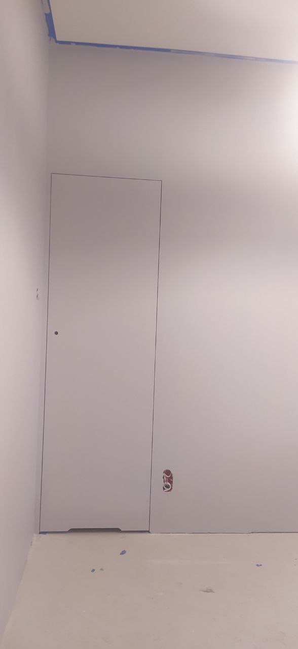 Świeżo pomalowane pomieszczenie z ukrytymi drzwiami i zabezpieczoną taśmą malarską górną krawędzią ściany oraz gniazdkiem elektrycznym w ścianie.