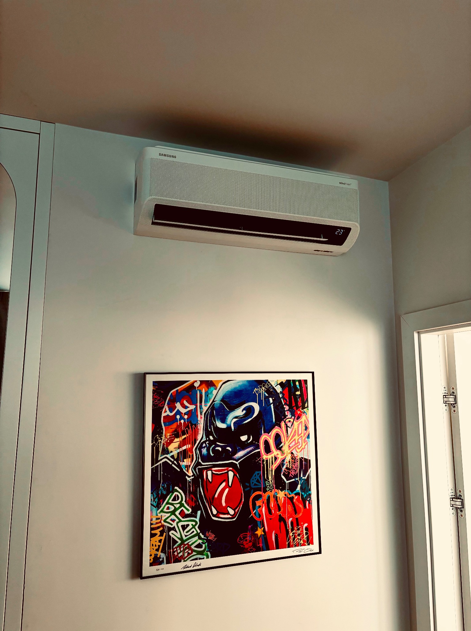 Biały klimatyzator Samsung WindFree na ścianie, pod nim grafika z gorylem w stylu graffiti. Nowoczesny design, temperatura 23 stopnie.