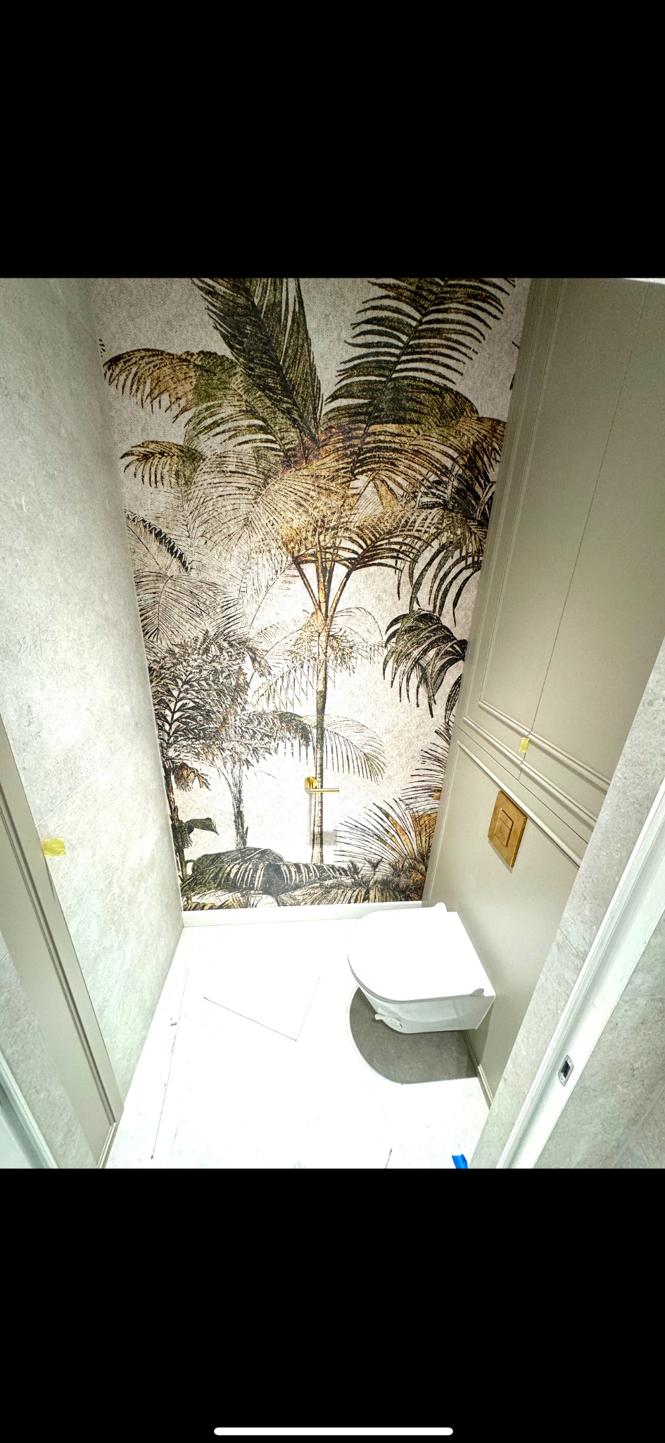 Wykończona łazienka z toaletą podwieszaną i tapetą z motywem tropikalnych palm na ścianie, widok z góry, białe płytki podłogowe.