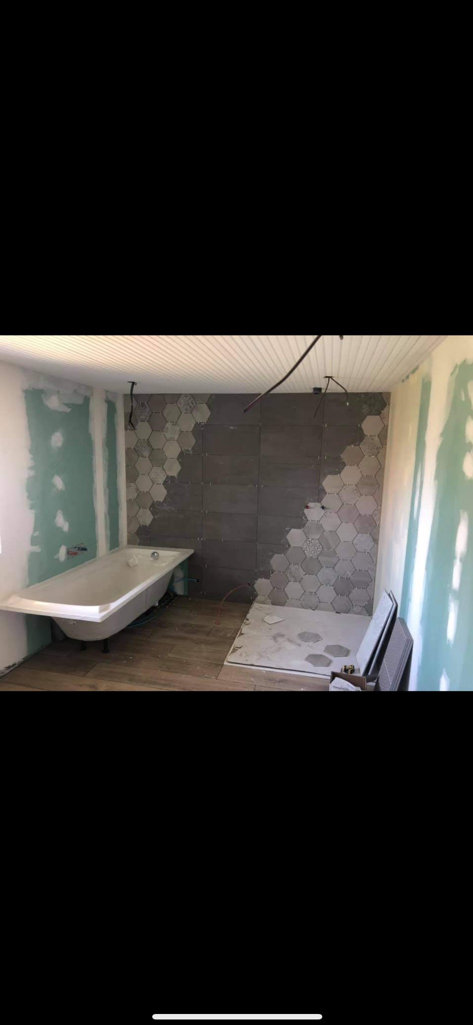Łazienka w trakcie remontu: częściowo ułożone heksagonalne płytki na ścianie, zamontowana wanna, podłoga wyłożona panelami imitującymi drewno, ściany przygotowane pod malowanie, widoczne kable