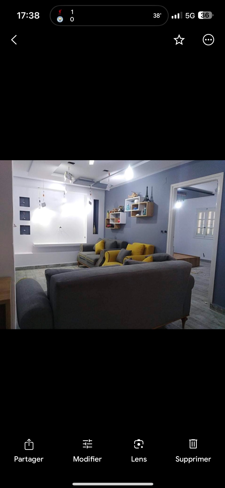 Szare ściany w salonie z szarymi sofami z żółtymi poduszkami, białe półki z dekoracjami i białe elementy dekoracyjne na ścianie.