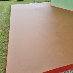 Przemek Staszewski - Beżowa, gładka powierzchnia wylewki na zewnątrz budynku, z widocznymi puszkami farb w tle, otoczona trawnikiem i zielenią.