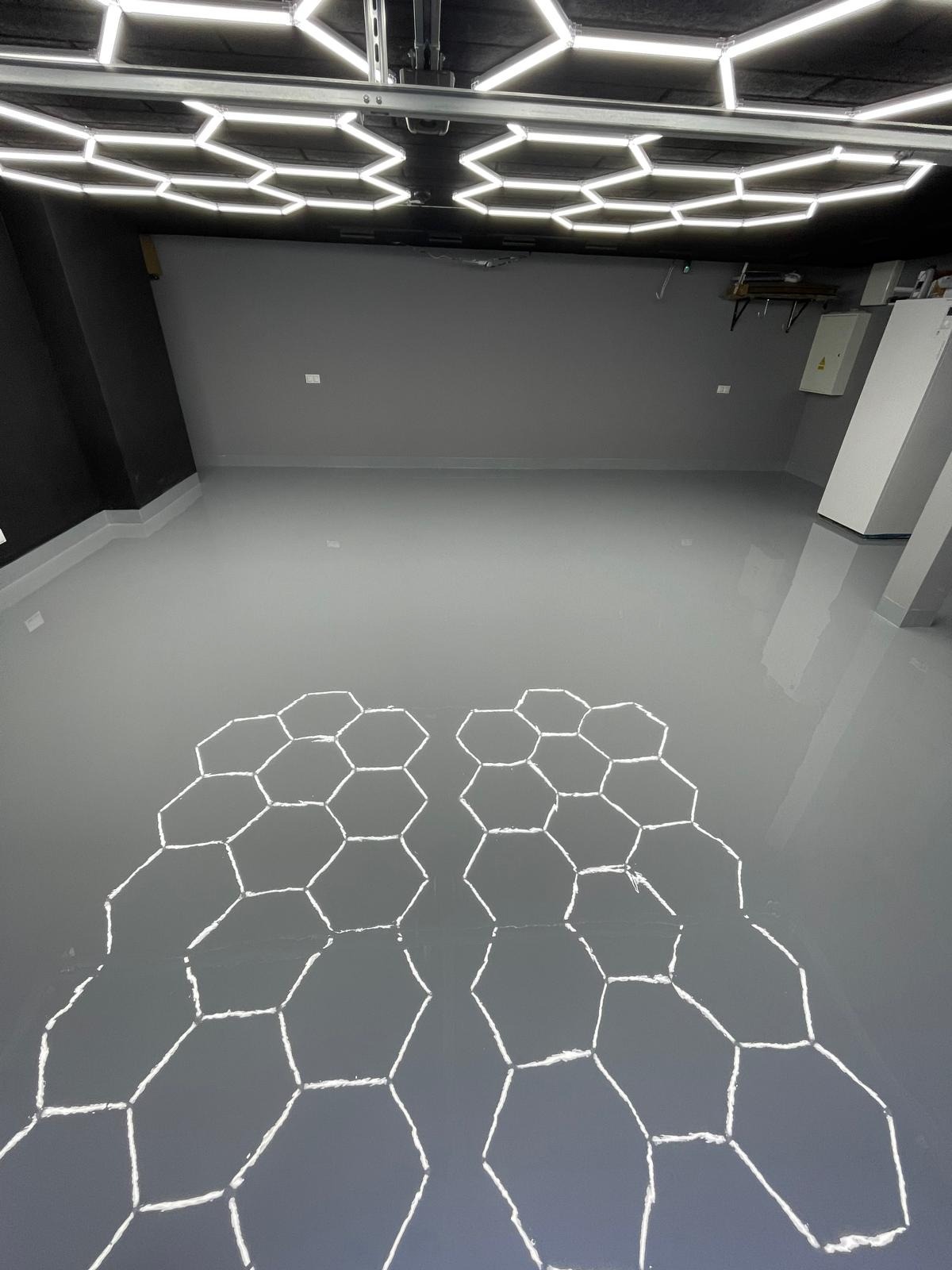 Gładka, szara posadzka z połyskiem, odbijająca heksagonalne lampy sufitowe, tworząc wzór plastra miodu.