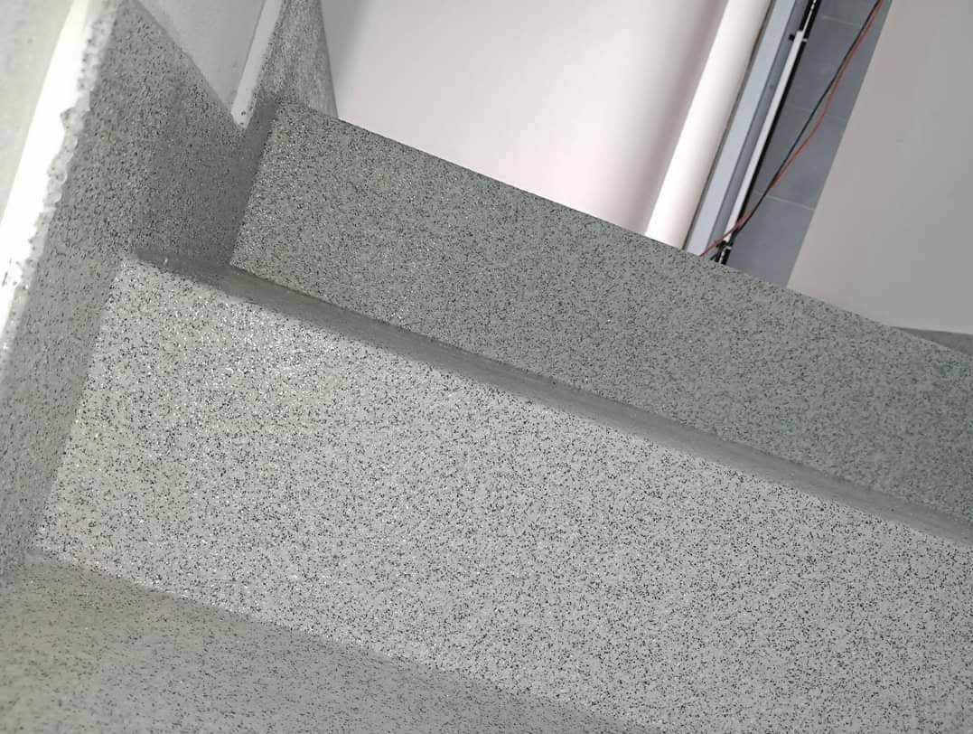 Schody wykończone szarą, nakrapianą powłoką, prawdopodobnie na bazie cementu, z widocznymi niedoskonałościami w narożnikach i krawędziach.