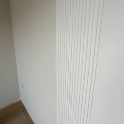 4domy - Biała ściana z dekoracyjnymi, pionowymi panelami ściennymi, widoczny fragment podłogi i ściana boczna w neutralnym odcieniu.