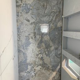 4domy - Płytka ścienna imitująca marmur w odcieniach szarości i błękitu, z kwadratowym odpływem liniowym umieszczonym centralnie, widoczna w narożniku łazienki z elementami konstrukcyjnymi półki wnękowej...