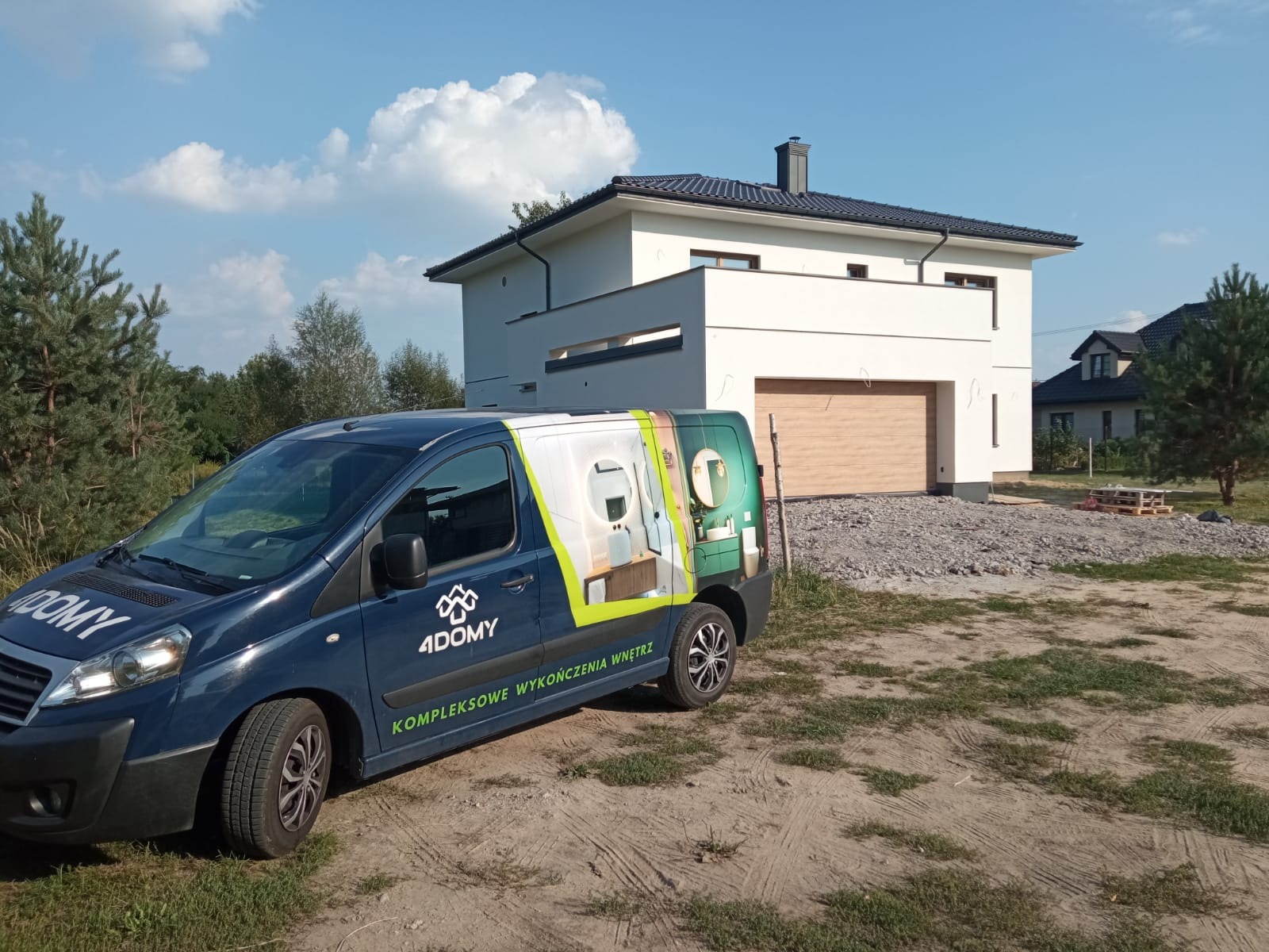 Niebieski samochód dostawczy z reklamą firmy wykończeniowej '4DOMY' na tle nowoczesnego, białego domu z brązową bramą garażową i szarym podjazdem z kamienia.