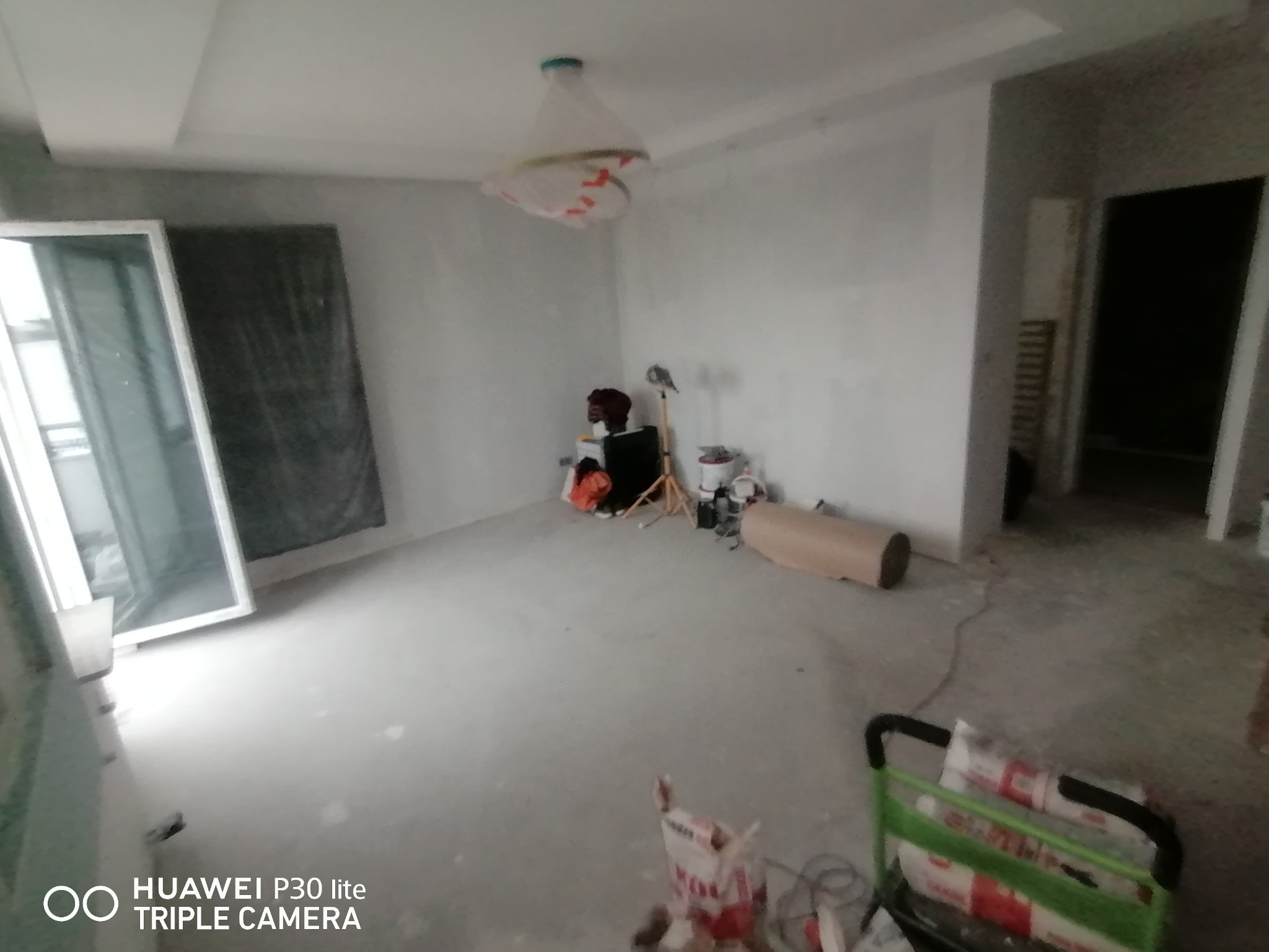 Pokój w trakcie remontu: ściany po szpachlowaniu, zabezpieczona lampa pod sufitem, widoczny karton i narzędzia, przygotowania do malowania.