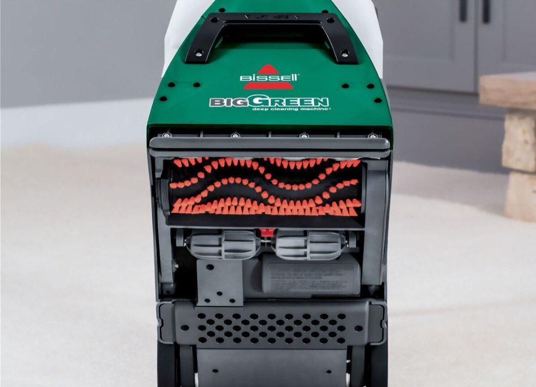 Zielony odkurzacz piorący Bissell Big Green z widoczną szczotką na tle jasnej podłogi i fragmentu szafki. Sprzęt do czyszczenia dywanów i tapicerki.