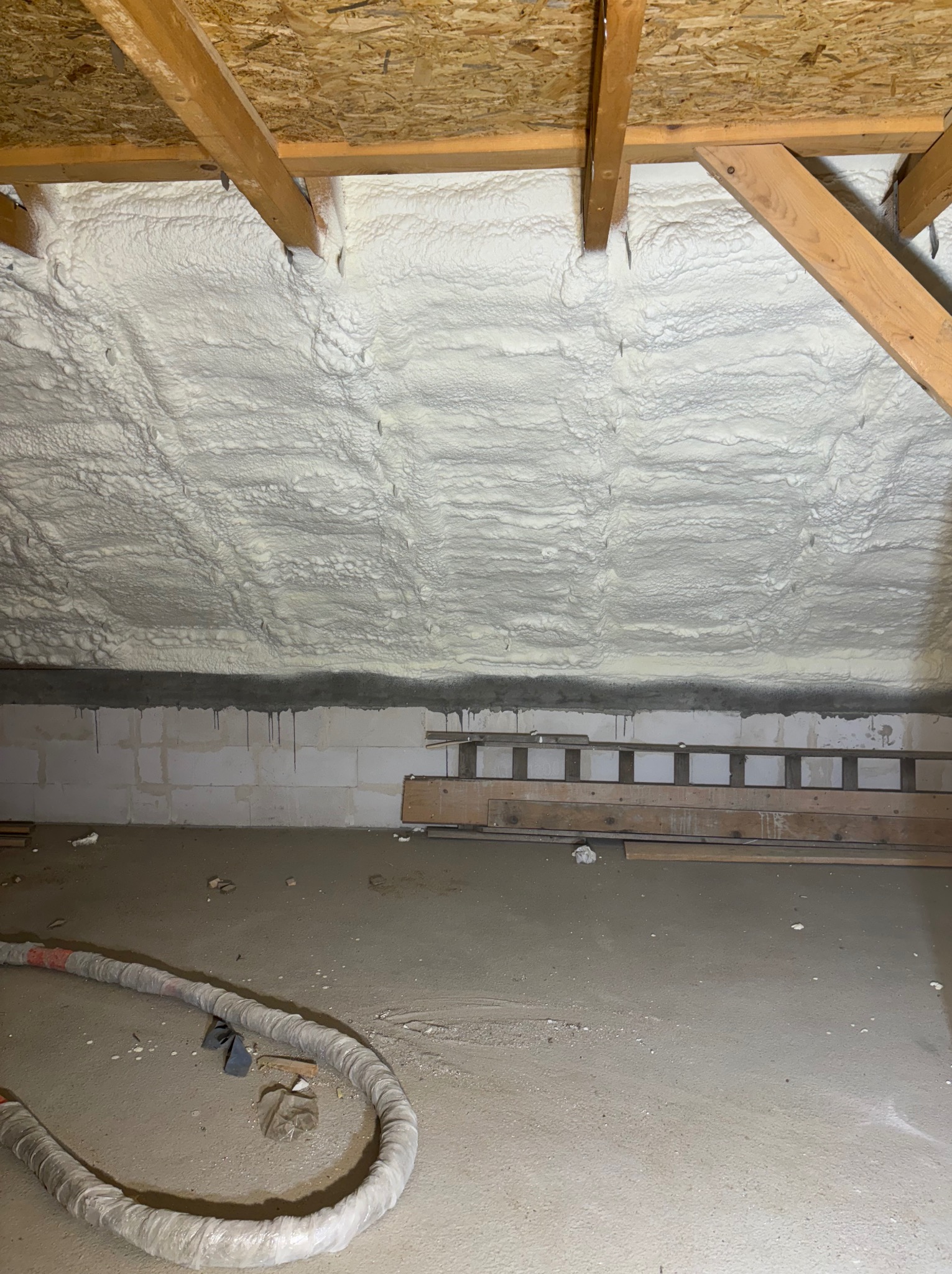 Poddasze po natrysku pianki izolacyjnej, widoczne krople skroplonej wody na ścianie z bloczków, na podłodze leży wąż do natrysku.