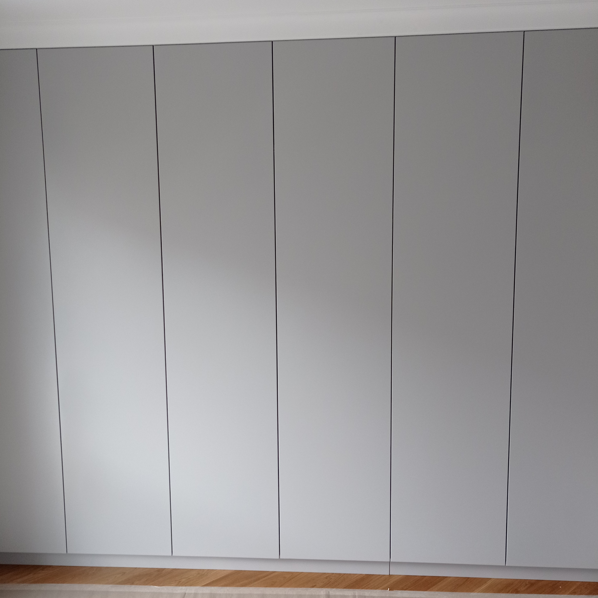 Szara szafa wnękowa z minimalistycznymi, gładkimi frontami, widoczna z perspektywy podłogi z parkietem.