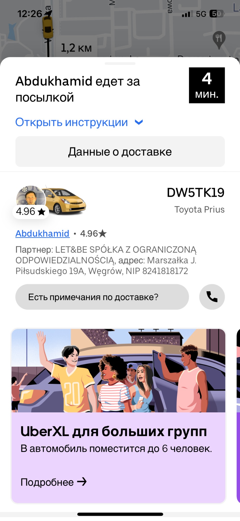 Ekran aplikacji Uber z informacją o kierowcy Abdukhamidzie, jego Toyocie Prius DW5TK19 i czasie dojazdu 4 minuty, poniżej reklama UberXL dla grup do 6 osób z ilustracją pasażerów wsiadających...