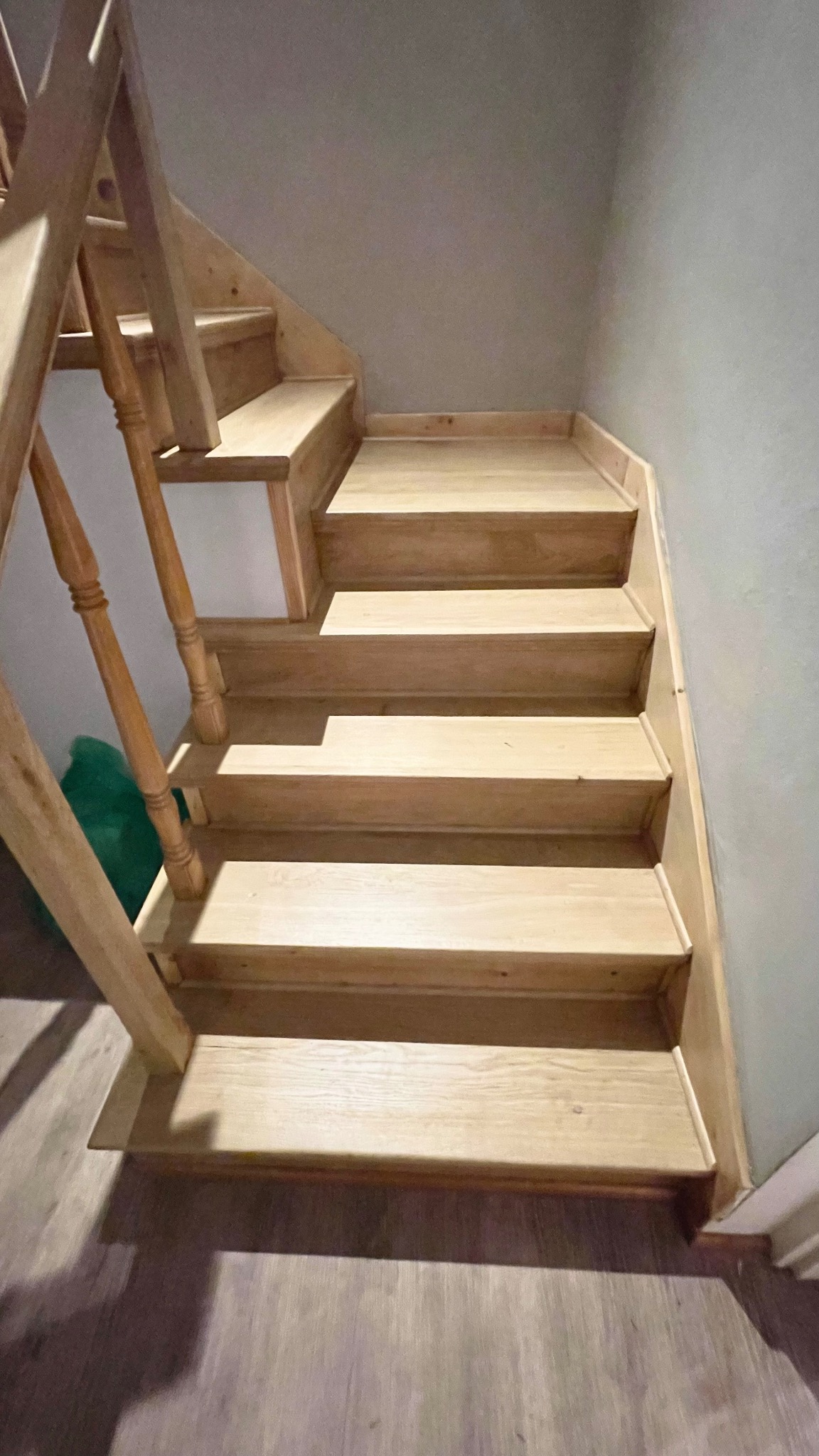 Jasne, drewniane schody po renowacji, widoczne z dołu, z delikatnym połyskiem i widoczną strukturą drewna.