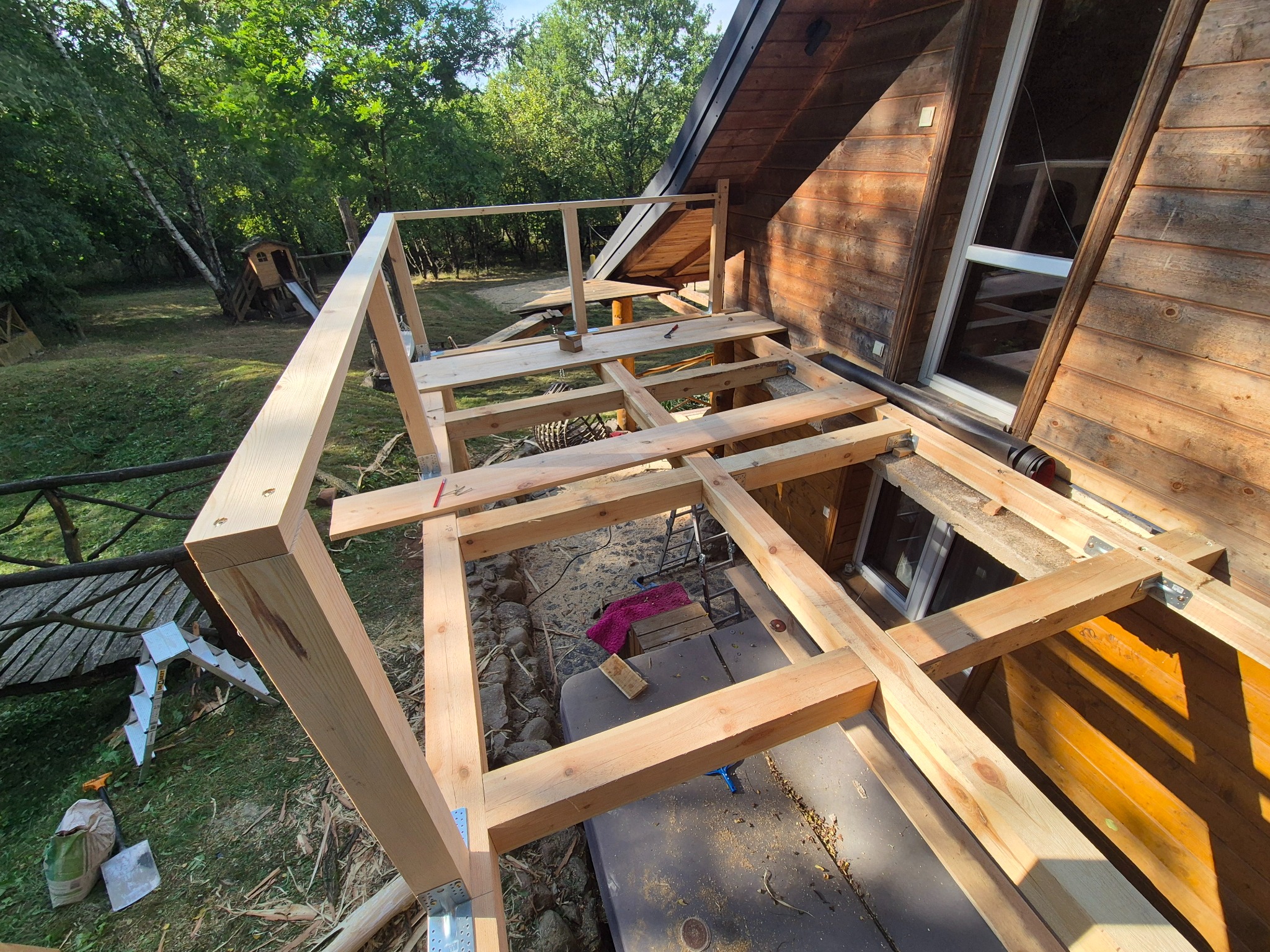 Konstrukcja drewnianego tarasu w Mszczonowie, widok z góry na szkielet z belek, mocowania metalowe. W tle dom z drewna i zieleń.