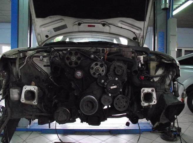 Widok z przodu na silnik samochodu bez przedniego pasa, z otwartą maską, w warsztacie na podnośniku.