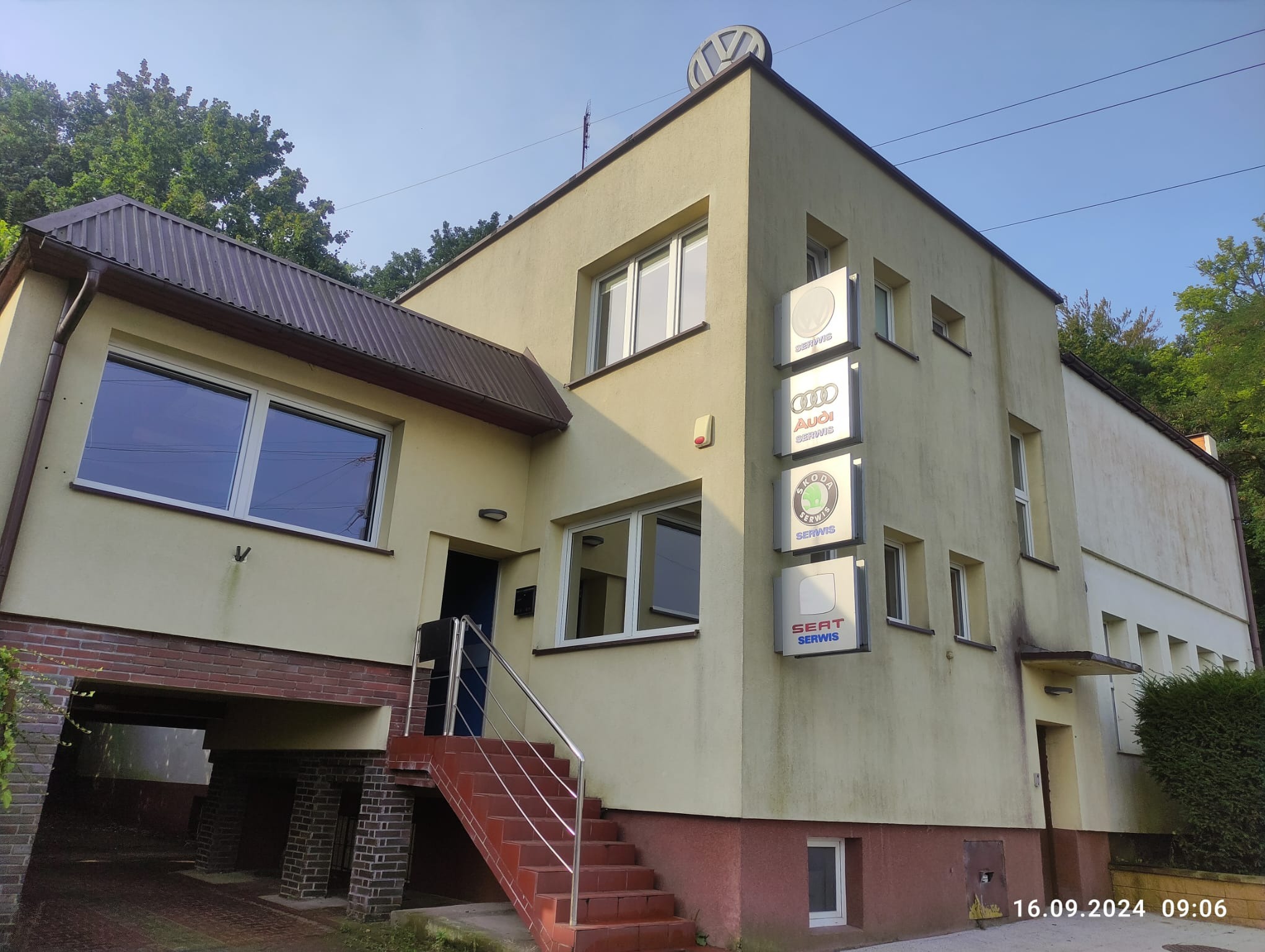 Budynek serwisu samochodowego z logo Volkswagen na dachu oraz szyldami Audi, Skoda i Seat przy wejściu.