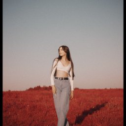 Mikołaj Musiałek Fotografia - Portret kobiety w plenerze na tle czerwonej trawy. Ubrana w biały top i jeansy, z długimi brązowymi włosami, odwraca wzrok w lewo. Delikatne światło, naturalny wygląd.