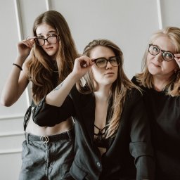 Mikołaj Musiałek Fotografia - Portret trzech kobiet w okularach na tle białej ściany. Różne style ubioru i wyraz twarzy. Rodzinna sesja w neutralnym oświetleniu.