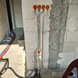 BarTech - Wewnętrzna instalacja elektryczna w trakcie montażu: przewody w peszlach wychodzą z pomarańczowych puszek w ścianie z betonu komórkowego. Widoczne oznaczenia schematu.