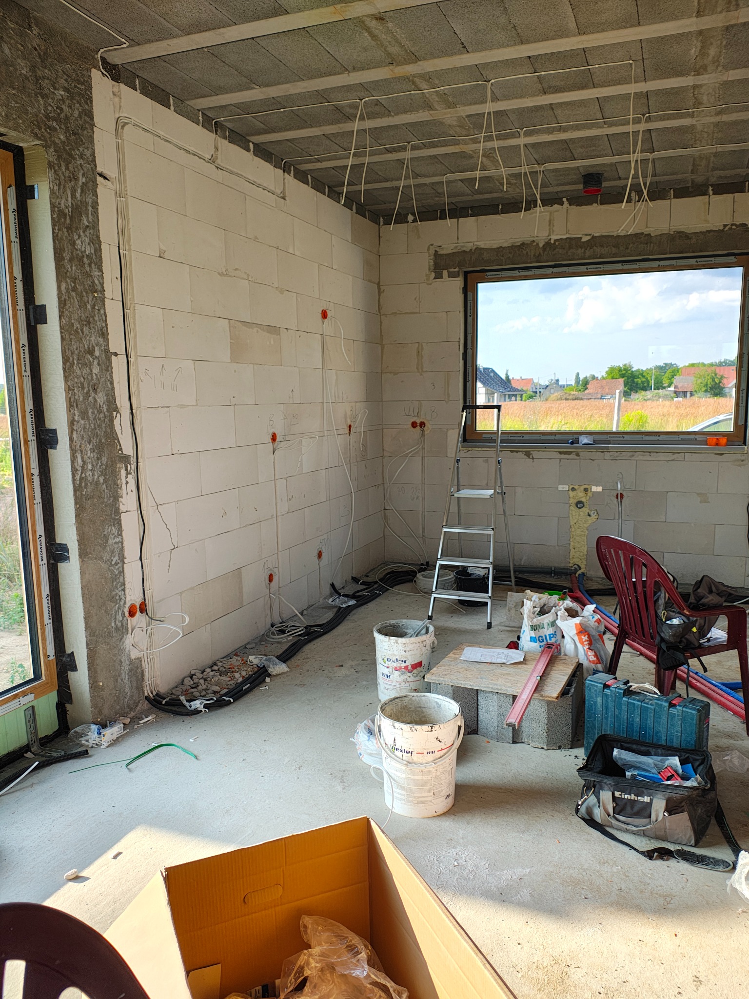 Surowy stan: instalacja elektryczna w budynku z betonu komórkowego. Kable wyprowadzone ze ściany, puszki instalacyjne. Widoczna drabina i narzędzia.
