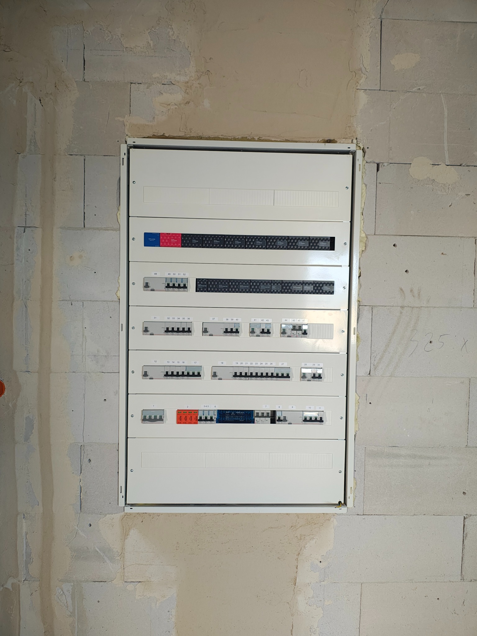 Rozdzielnica elektryczna, zamontowana na surowej ścianie z betonu komórkowego, widok z przodu, instalacja w trakcie prac wykończeniowych.