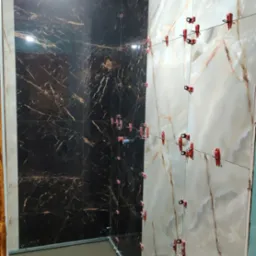 Proces układania płytek w łazience, widoczne płytki imitujące marmur w dwóch kolorach - ciemnym i jasnym, oraz system poziomowania płytek z czerwonymi klipsami i sznurkiem.