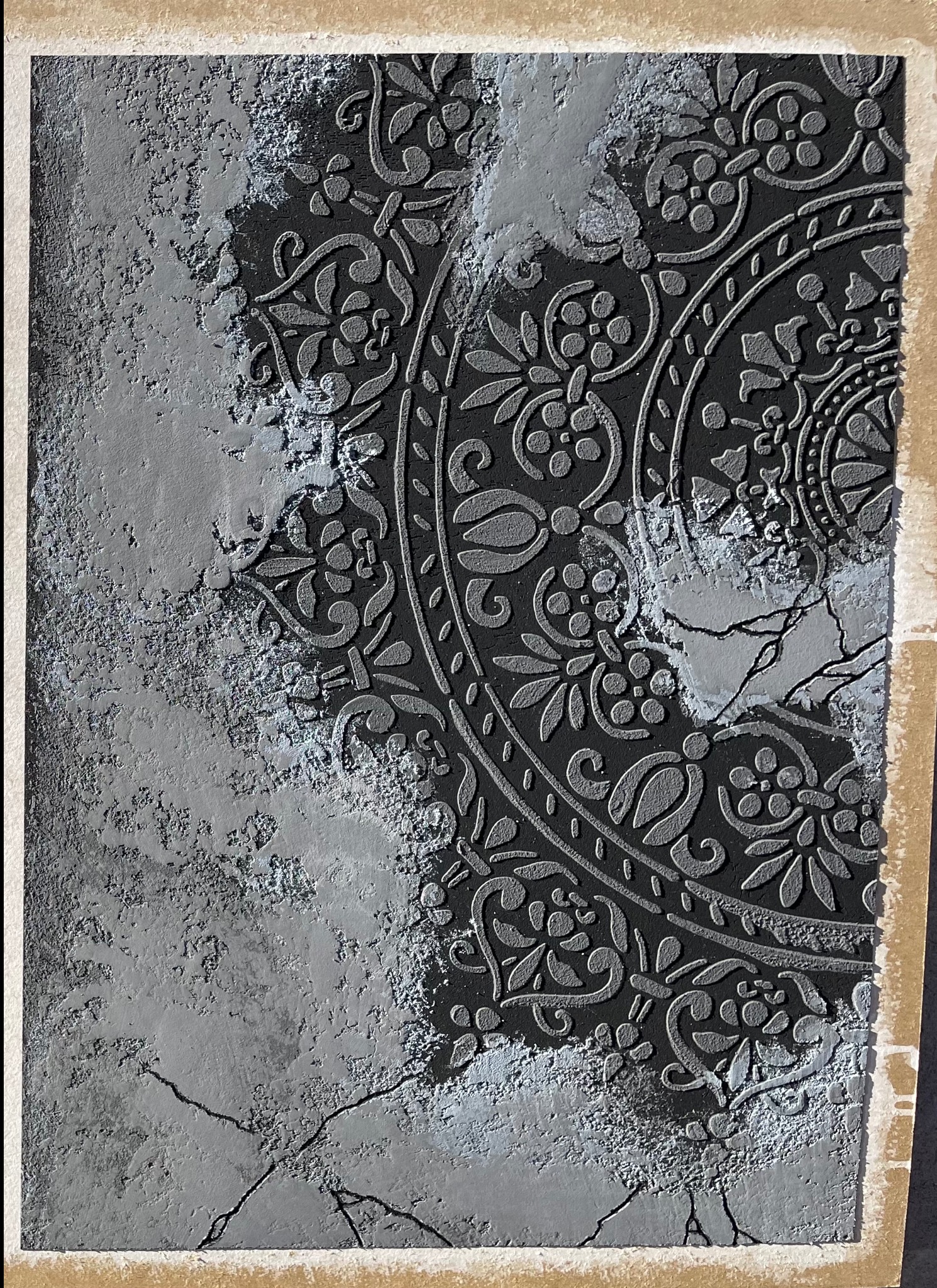 Dekoracyjna ściana z efektem reliefu i wzorem mandali, częściowo pokryta szpachlą imitującą spękania. Czarno-szara kolorystyka, zbliżenie na detal faktury.