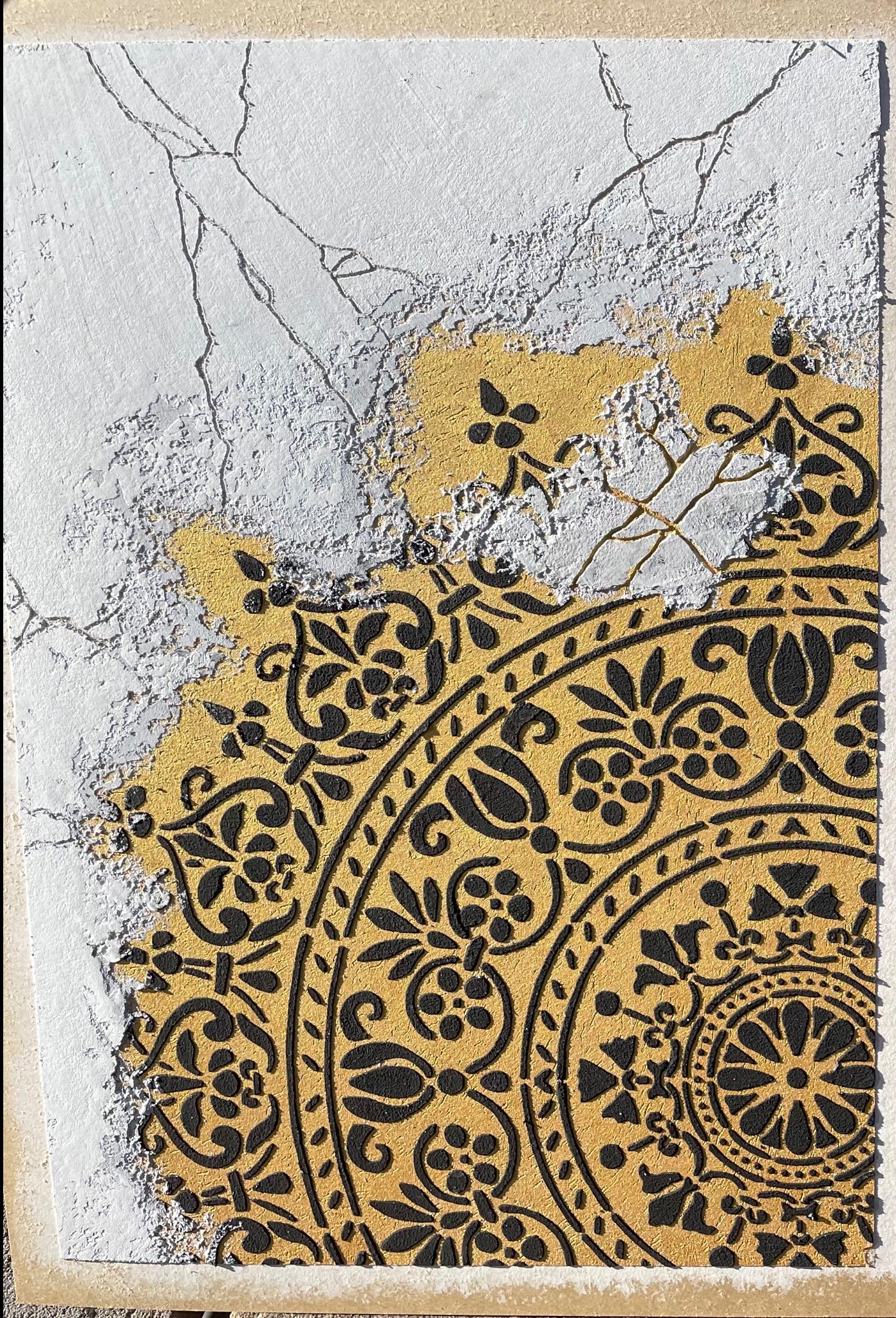 Fragment dekoracyjnej ściany z efektem spękań i złoconym, orientalnym wzorem nałożonym na nierówną, białą powierzchnię. Unikalna faktura i kontrast kolorów.