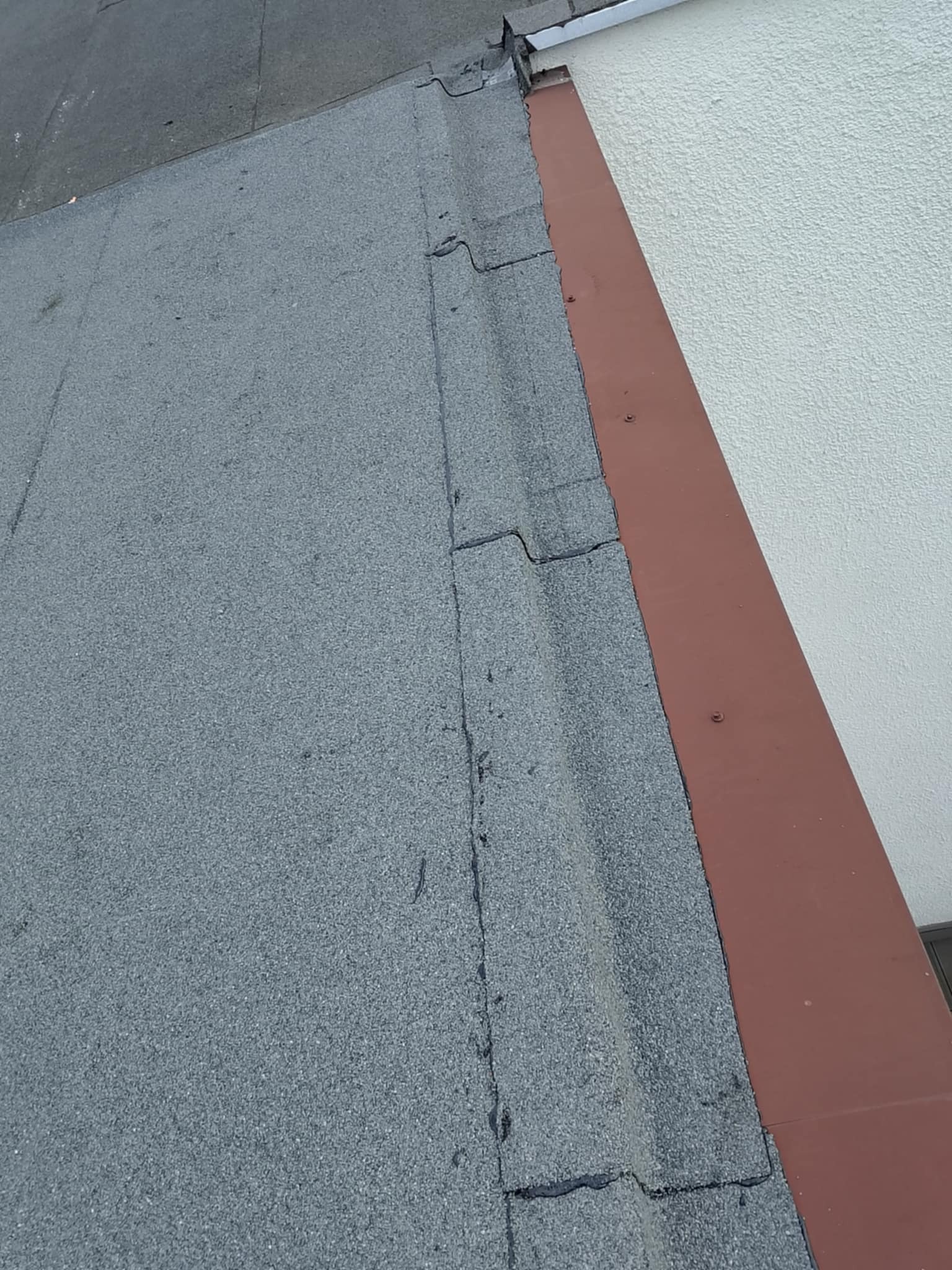 Szczegółowe ujęcie dachu pokrytego papą w Łasinie, z widocznym fragmentem ściany i obróbką blacharską. Układ papy z wyraźnymi łączeniami.