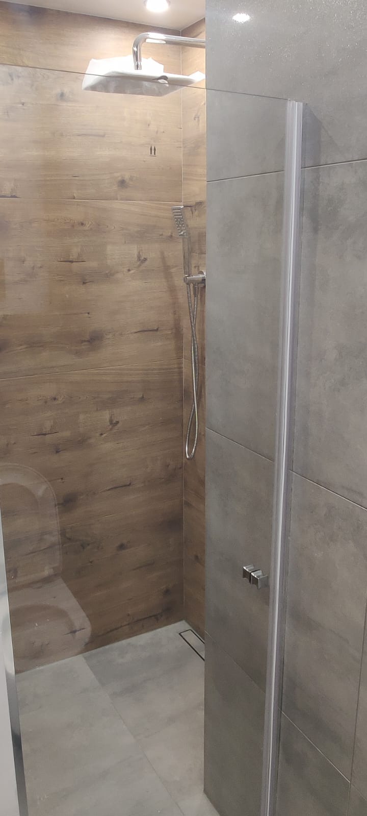 Nowoczesna kabina prysznicowa walk-in z drewnopodobnymi i szarymi płytkami w Bytomiu. Widoczny odpływ liniowy i deszczownica. Minimalistyczny design.