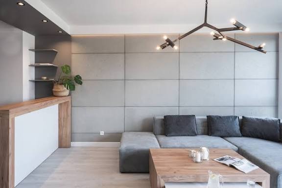 Minimalistyczny salon z szarą ścianą z paneli, drewnianym stolikiem kawowym i designerską lampą sufitową.