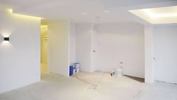 Białe, minimalistyczne wnętrze po remoncie. Ściany pomalowane na biało, nowoczesne oświetlenie punktowe i dekoracyjne. Widoczne puszki po farbie, przewód na podłodze.